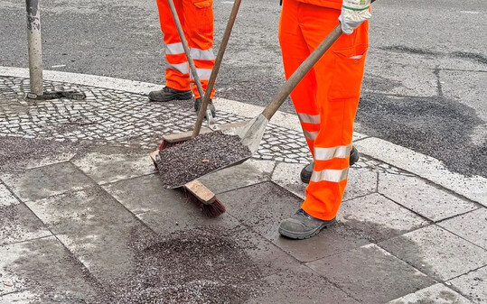 Mitarbeiter reinigen einen Gehweg von Splitt aus dem Winter.