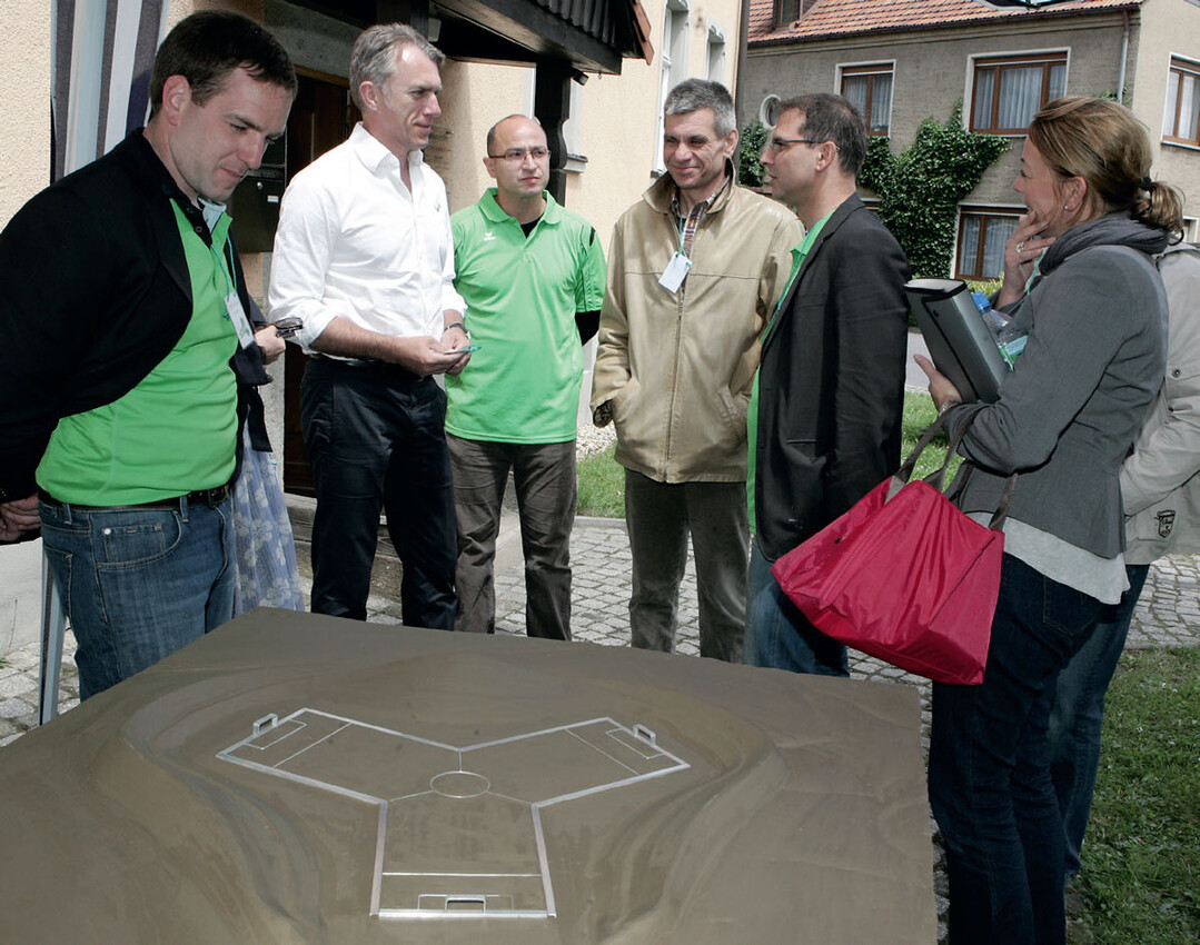 2010 bei der 3kick-Premiere in Kirschau: (v. l.) Architekt Ludwig Pickert, die Künstler Neo Rauch und Sandro Porcu, Sven Gabriel, Bürgermeiser der Stadt Kirschau, und Presseleute am Ton-Modell des Spielfelds