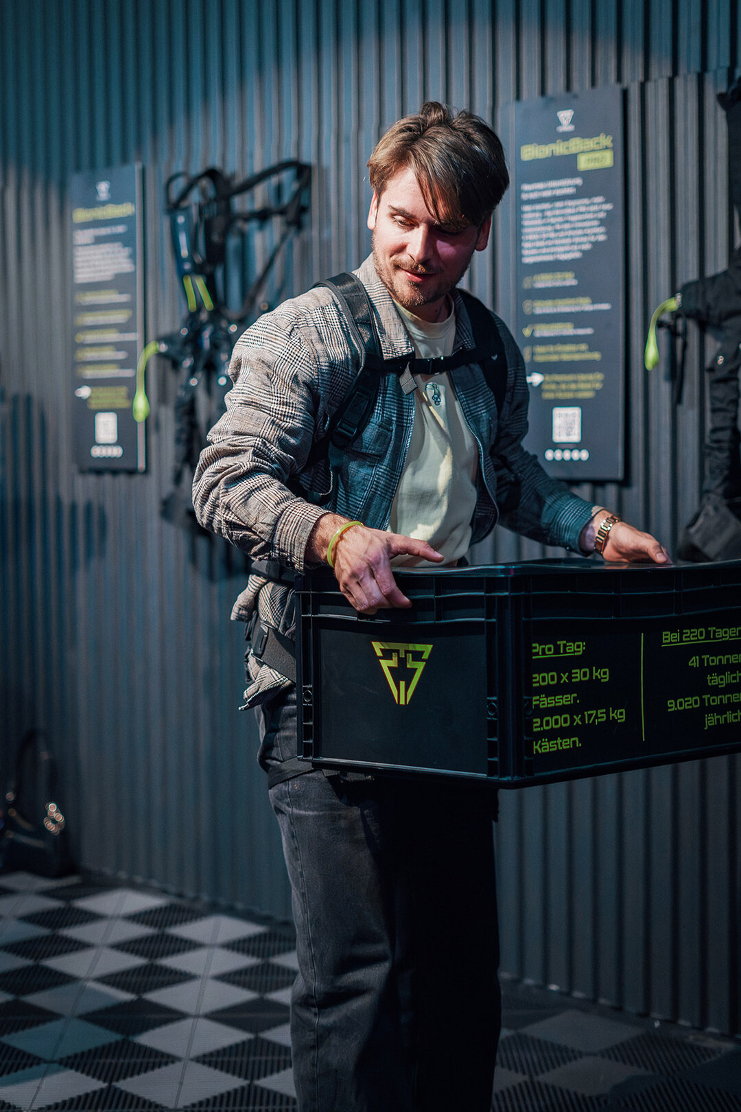 Gast testet im Showroom bei der Firmeneinweihung das BionicBack und hebt eine Kiste.